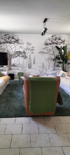 A room with a green carpet, a brown chair, a television, and a wall with a nature-themed mural. - AIR-CONDITIONED PROVENCAL VILLA WITH A POOL AND SPA ON THE WAY TO BIOT   (Antibes)