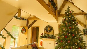 Een gezellige woonkamer met een grote kerstboom, een open haard en een trap versierd met guirlandes.