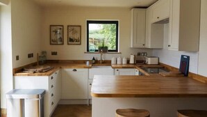 Een moderne keuken met houten aanrechtbladen, witte kasten en een raam met uitzicht op groen.