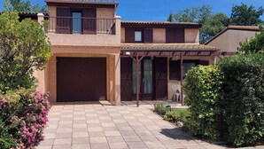 Une maison à deux étages dotée d’un patio couvert, d’un garage et d’un jardin agrémenté de plantes à fleurs.