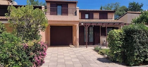 A two-story house with a covered patio, a garage, and a garden with flowering plants. - Spacious air-conditioned house, estate with swimming pools and activities, close to the sea (Portiragnes)
