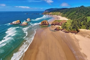 Eine Küstenlandschaft mit Sandstrand, Felsformationen und dicht bewaldeten Hügeln.