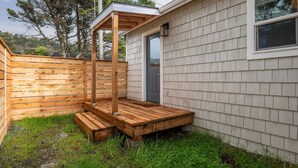 A wooden deck with a pergola, a door, and a window on a house with siding. - Coral Cottage Unit #1: Walk to Beach, Pet Friendly (Rockaway Beach)