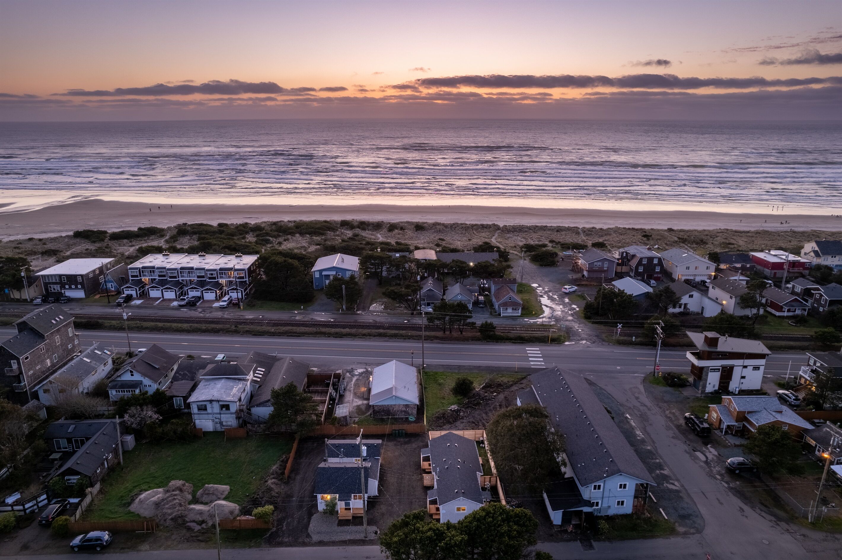 An aerial view of a coastal residential area with houses, a road, and a beach.