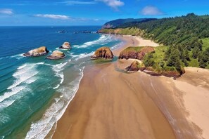 Un paisaje costero con una playa arenosa, afloramientos rocosos y colinas boscosas.
