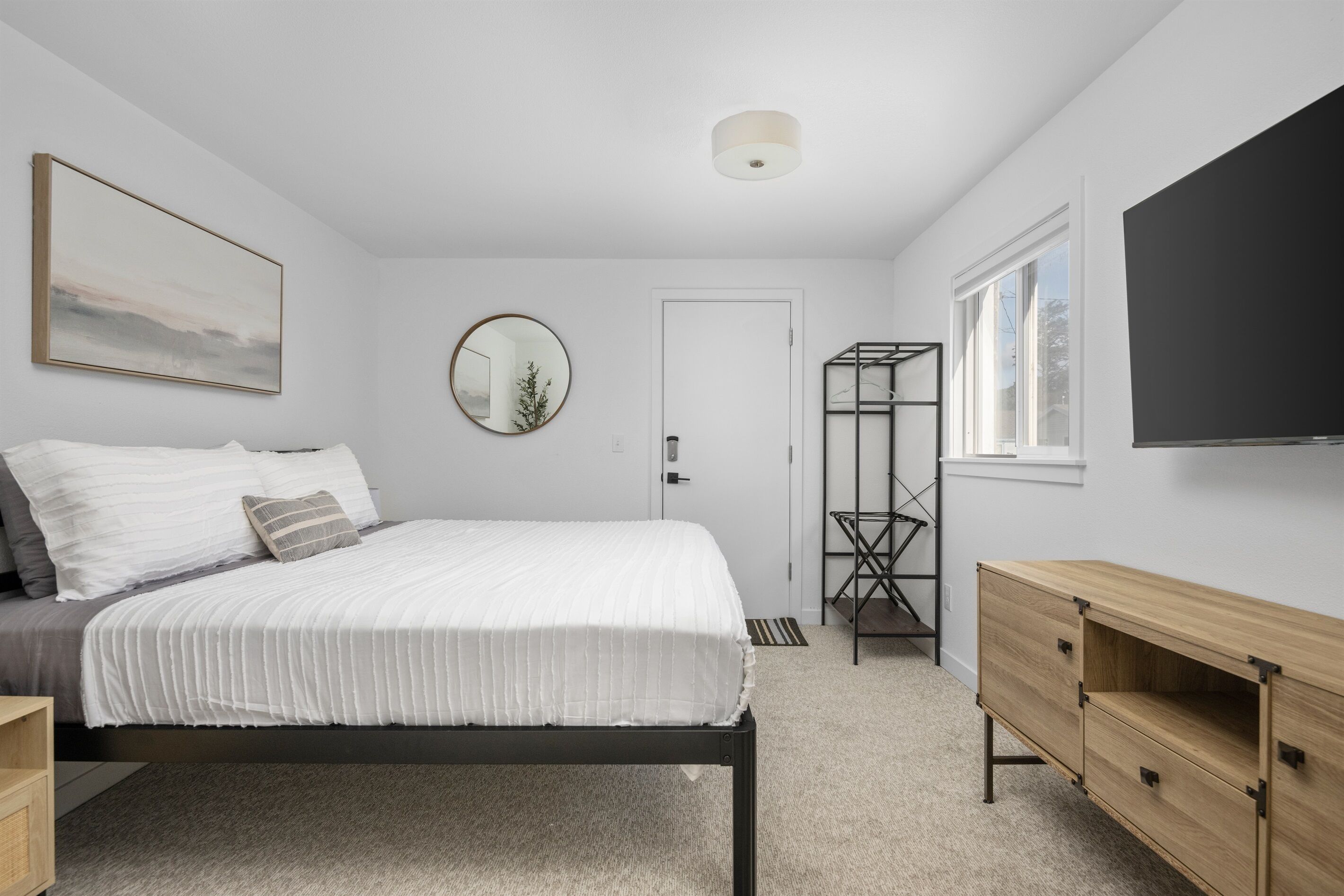 A bedroom with a bed, a bedside table, a dresser, a mirror, a window, and a door.