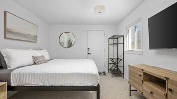 A bedroom with a bed, a bedside table, a dresser, a mirror, a window, and a door.