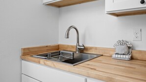 A modern kitchen with a stainless steel sink, wooden countertop, and white cabinetry. - Inn at Rockaway Beach #1: Walk to Beach, Pets OK (Rockaway Beach)
