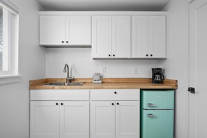 Eine kleine Küche mit weißen Schränken, einer Holz Arbeitsplatte, einem Spülbecken, einer Kaffeemaschine und einem türkisblauen Kühlschrank.