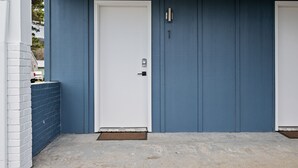 A blue exterior wall with two white doors, a metal gate, and a concrete ground. - Inn at Rockaway Beach #1: Walk to Beach, Pets OK (Rockaway Beach)