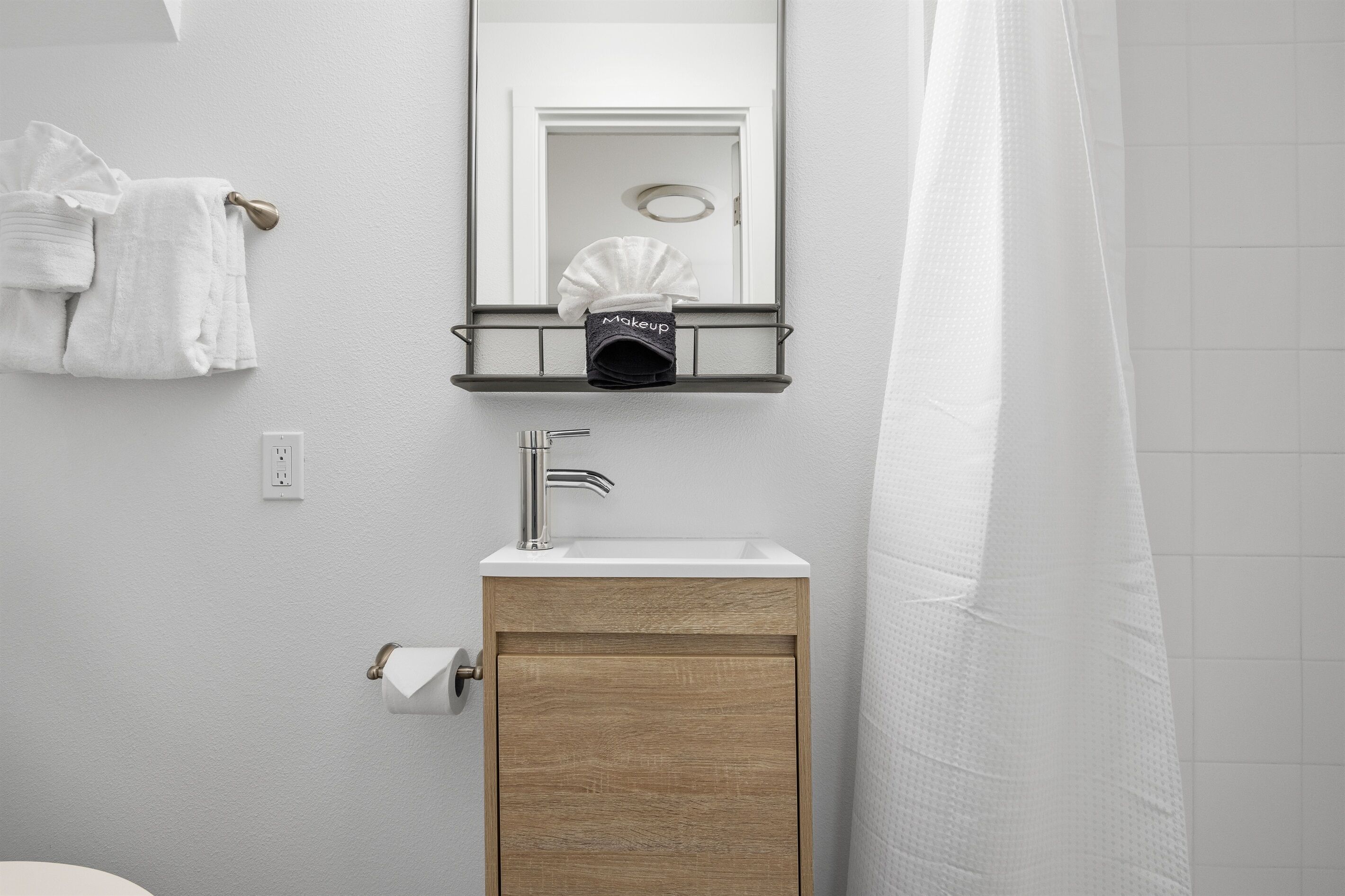 Un baño con lavamanos, espejo, toallero y cortina de ducha.