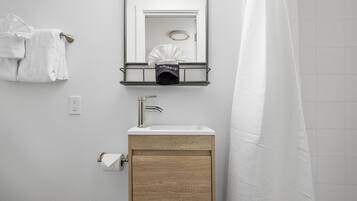 Un baño con lavamanos, espejo, toallero y cortina de ducha.