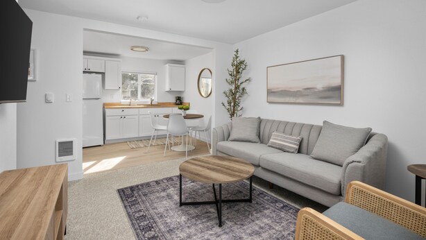 Una sala de estar moderna con un sofá gris, una mesa de centro de madera y un comedor con sillas blancas.