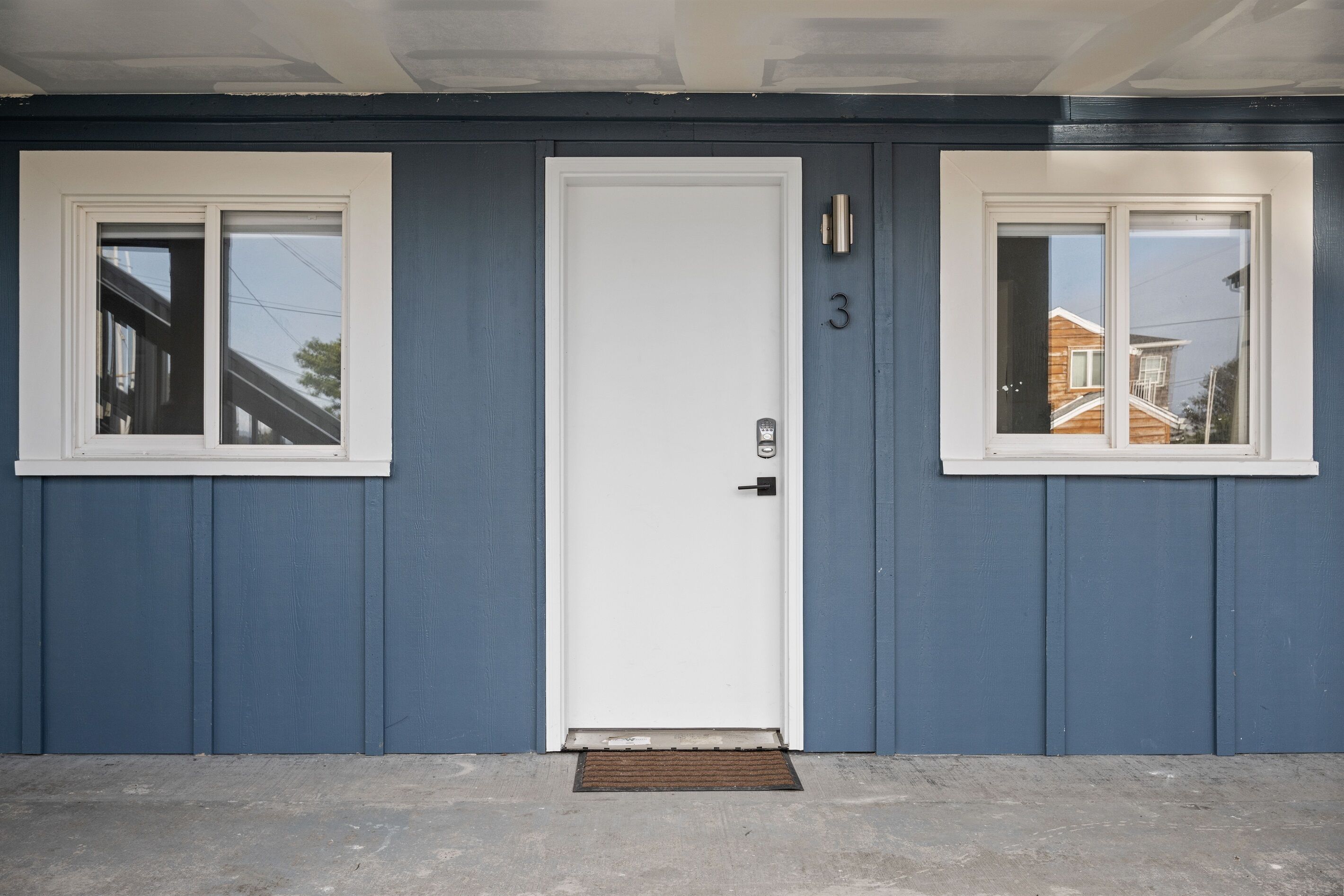 A blue house with a white door and two windows, each with a white frame.