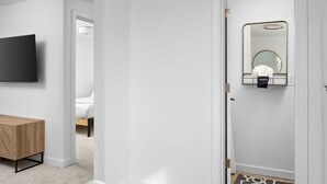 Un dormitorio moderno con una cama, un televisor, una mesita de noche de madera y un espejo con una toalla colgada.