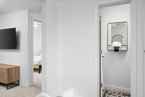 A modern bedroom with a bed, a TV, a wooden bedside table, and a mirror with a towel hanging on it.