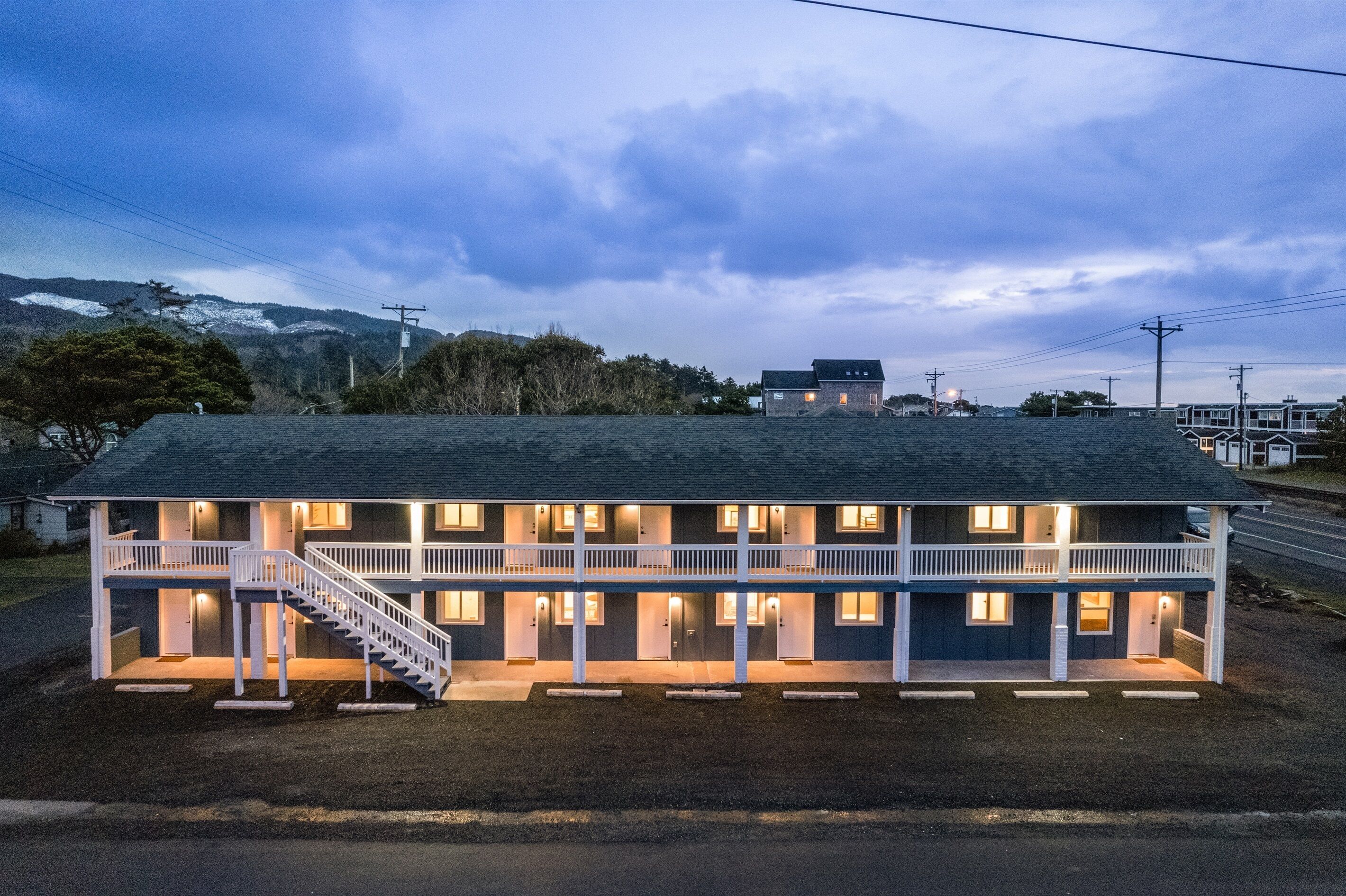 Un motel de dos pisos con una escalera central, varias habitaciones y vistas del paisaje circundante.