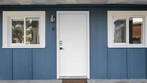 Ett hus med en vit dörr och två fönster, båda med vita fönsterramar.