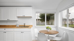 Eine moderne Küche mit weißen Schränken, einer Holzauskleidetheke und einem Essbereich mit einem runden Tisch und weißen Stühlen.