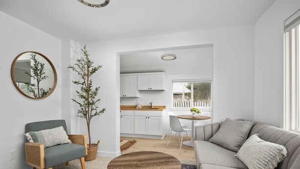 Ein modernes Wohnzimmer mit einem grauen Sofa, einem runden Couchtisch, einem Korbstuhl und einer Topfpflanze.