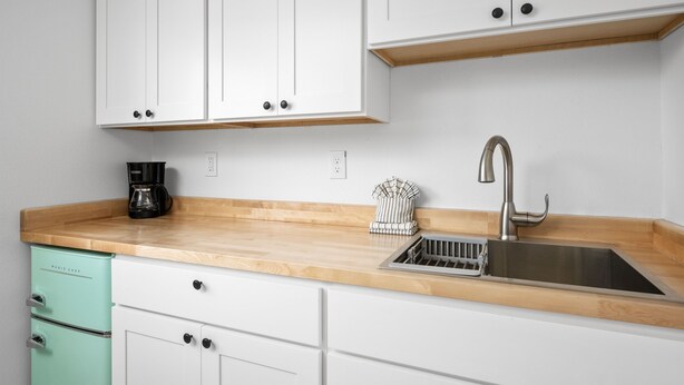A kitchen with white cabinets, a stainless steel sink, a coffee maker, and a vintage-style dish rack. - Inn at Rockaway Beach #6: Walk to Beach, Pets OK (Rockaway Beach)