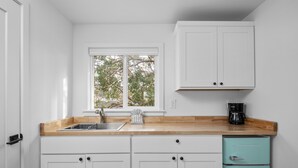 Una cocina con armarios blancos, encimera de madera, un fregadero y una cafetera.
