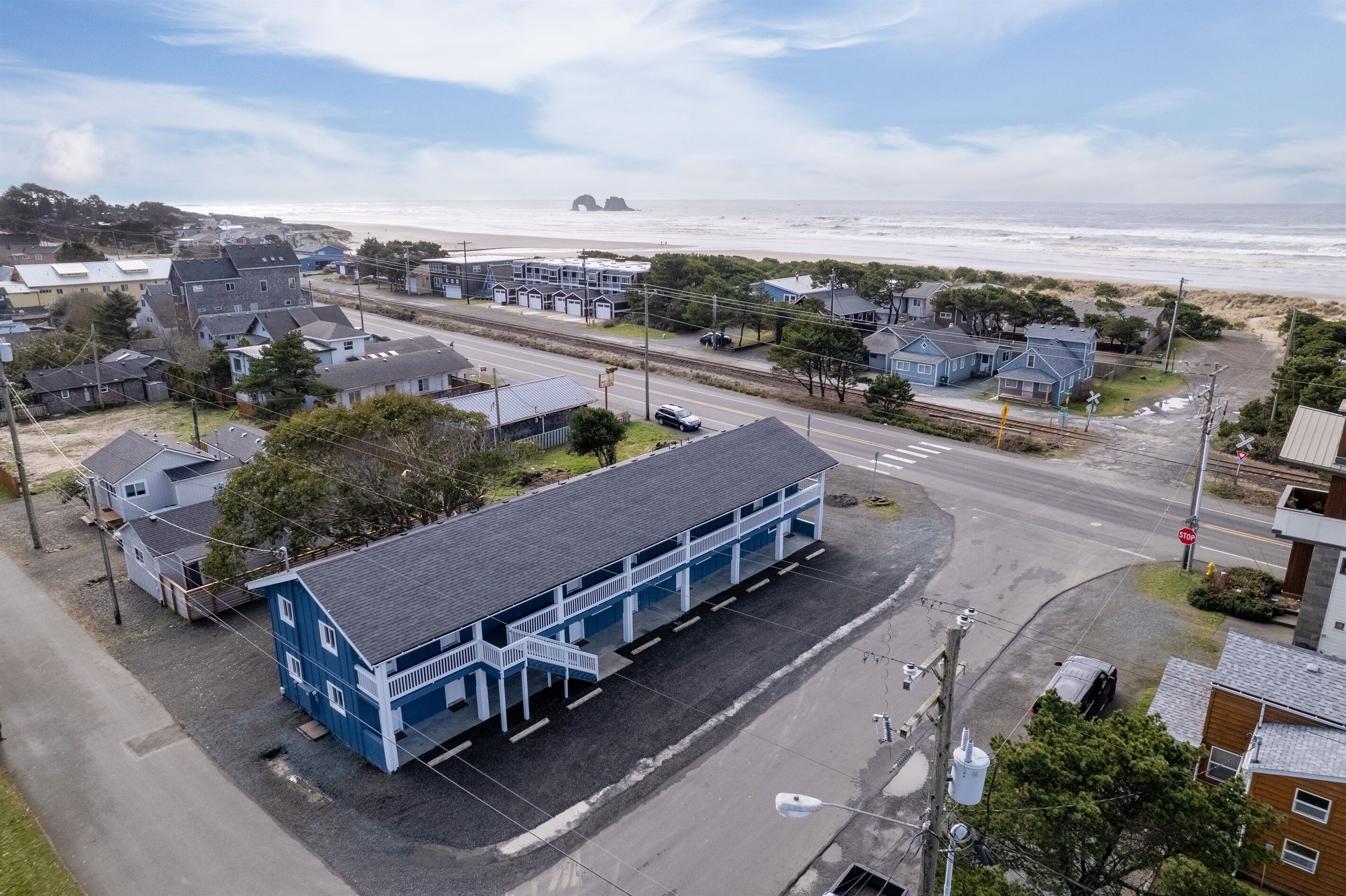 A coastal town with a prominent blue building with a balcony, a beach in the background, and a road leading to it.