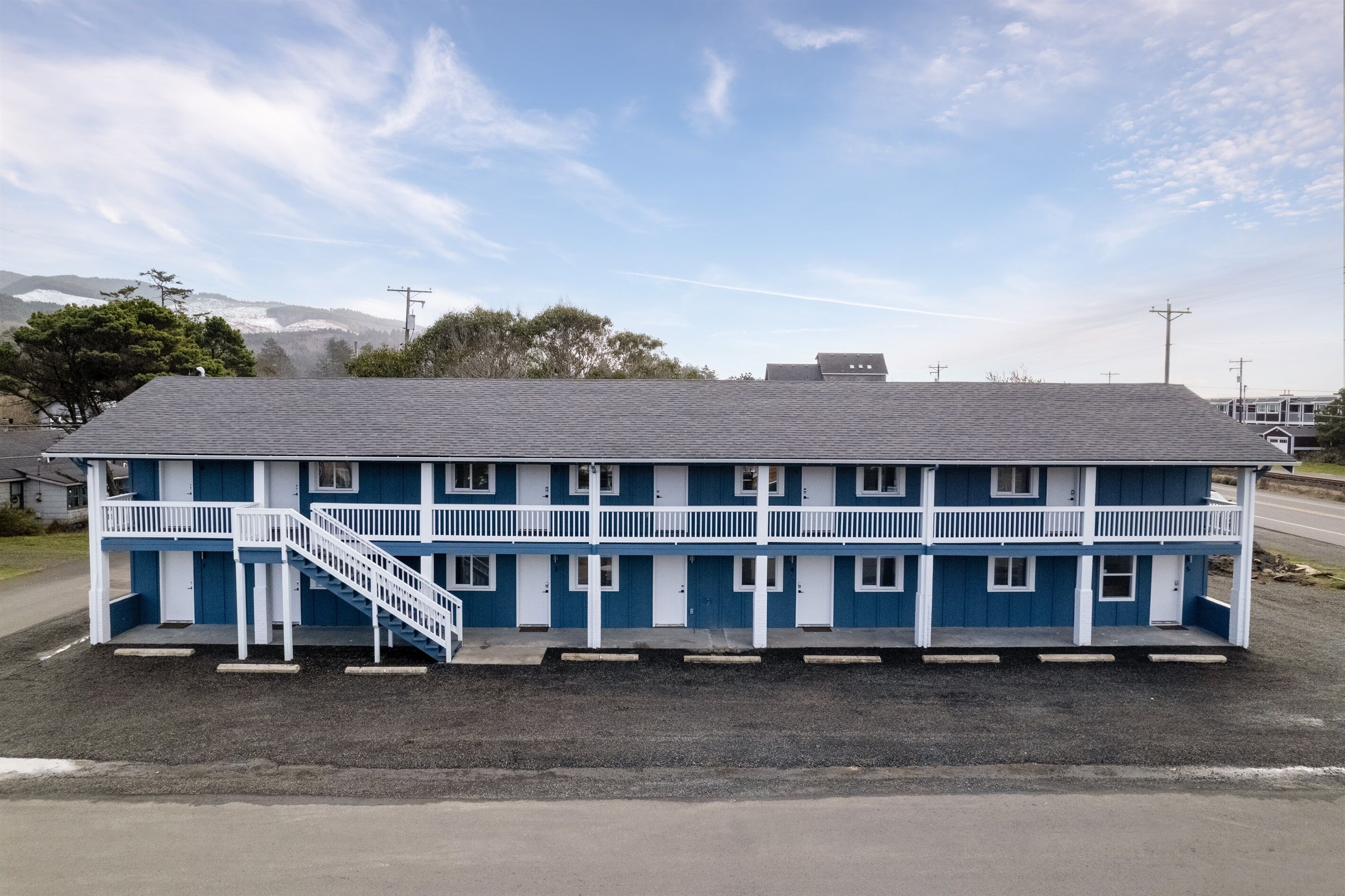 A two-story motel with a blue exterior and white trim, featuring a central staircase and a covered front porch.