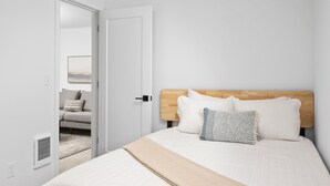 A bedroom with a bed, a wooden headboard, a white wall, a door, and a small window. - Inn at Rockaway Beach #9: Walk to Beach, Pets OK (Rockaway Beach)