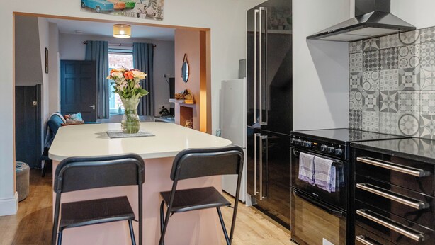 Een kleine keuken met een centraal eiland, twee barkrukken, een koelkast en een ingebouwde oven.