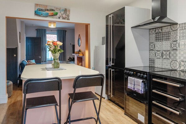 A compact kitchen with a central island, two bar stools, a refrigerator, and a built-in oven. - Cosy Home From Home | Walk to Centre | Free Parking (York)