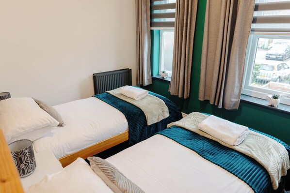 Habitación de hotel con dos camas, una ventana con cortinas, un radiador y una planta pequeña en el alféizar.