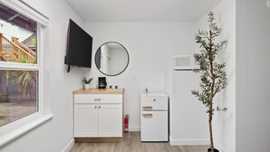 A compact kitchen with white cabinetry, a black countertop, a round mirror, a white refrigerator, and a potted plant. - Ocean Rogue Inn Suite #10 - Suite | Oceanfront (Rockaway Beach)