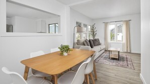 En moderne stue med et træspisebord, hvide stole, en grå sofa og et lille sofabord.