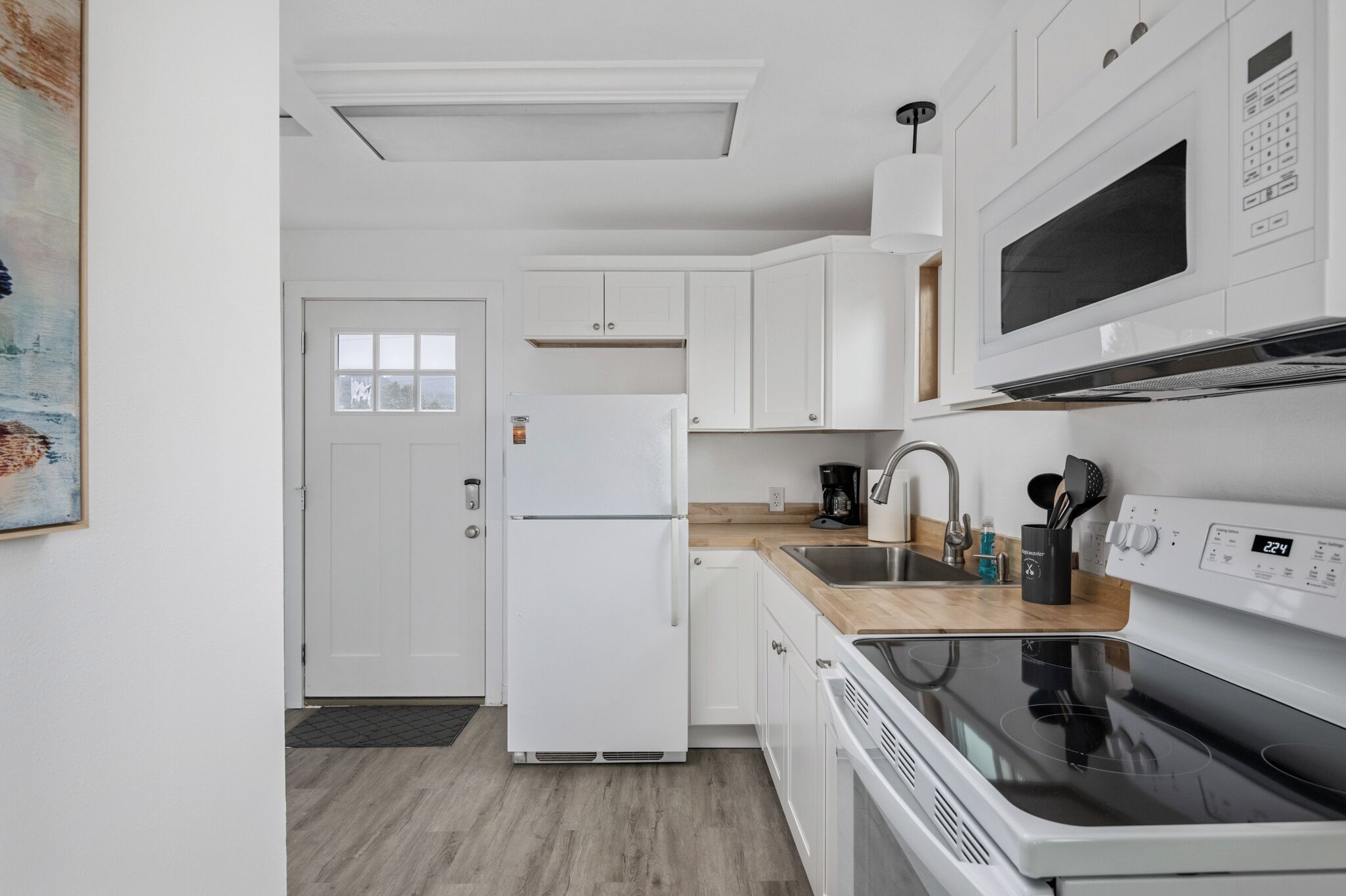 A modern kitchen with white cabinets, a stainless steel sink, a microwave, and a stove.