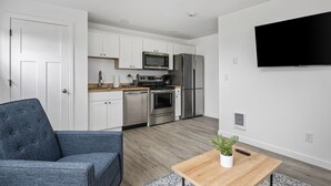 Eine moderne Küche mit Edelstahlgeräten, einem Flachbildfernseher und einer Sitzecke mit blauem Sofa und Holztisch.