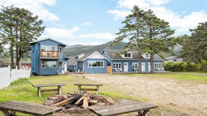 A row of blue houses with a fire pit and benches in the foreground. - Ocean Rogue Inn Suite #4 - 1 BD Condo | Oceanfront (Rockaway Beach)