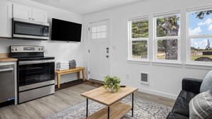 A modern kitchen with stainless steel appliances, a flat-screen TV, and a wooden bench. - Ocean Rogue Inn Suite #4 - 1 BD Condo | Oceanfront (Rockaway Beach)