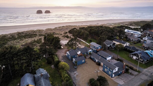 An aerial view of a coastal residential area with houses, a beach, and rocky outcrops. - Ocean Rogue Inn Suite #4 - 1 BD Condo | Oceanfront (Rockaway Beach)