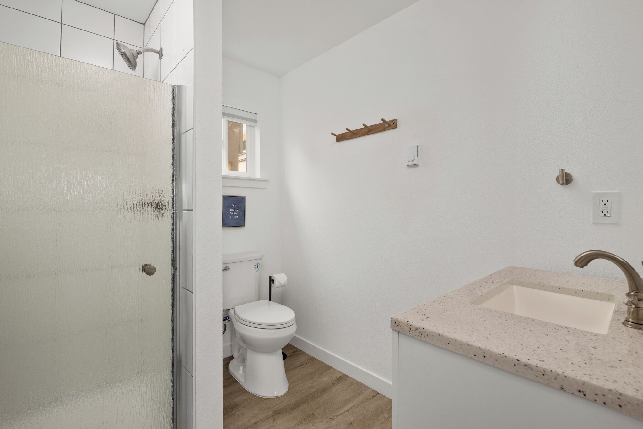 Et badeværelse med et hvidt toilet, en vask med marmoreret bordplade og et træklædeskab.