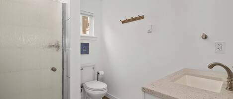 Et badeværelse med et hvidt toilet, en vask med marmoreret bordplade og et træklædeskab.