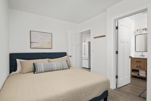 Ein Schlafzimmer mit einem Bett, einem Nachttisch, einem Spiegel und einer Tür zu einem Badezimmer.