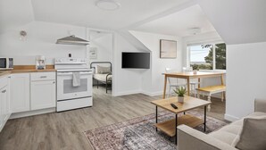 A modern kitchen with white cabinetry, a built-in oven, and a microwave. There is a dining area with a wooden table and chairs, and a large window providing natural light.