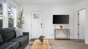 A modern living room with a grey sofa, a wooden coffee table, a TV on a stand, and a door with a window.