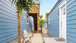 A narrow outdoor space with a wooden deck, a chair, and a palm tree.