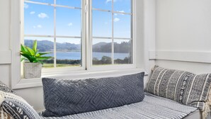 En sittplats vid fönstret med utsikt över en sjö och kullar, en krukväxt och mönstrade kuddar.
