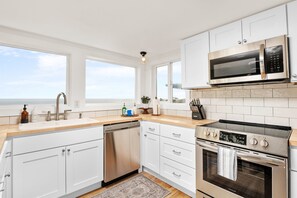 A modern kitchen with white cabinets, stainless steel appliances, a dishwasher, and a view to the outside. - Beautiful Oceanside Retreat: 7 Bedrooms, Hot Tub, Views, Sleeps Big Groups (Oceanside)