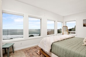 Ein Schlafzimmer mit Bett, Sessel und Blick auf das Meer durch große Fenster.