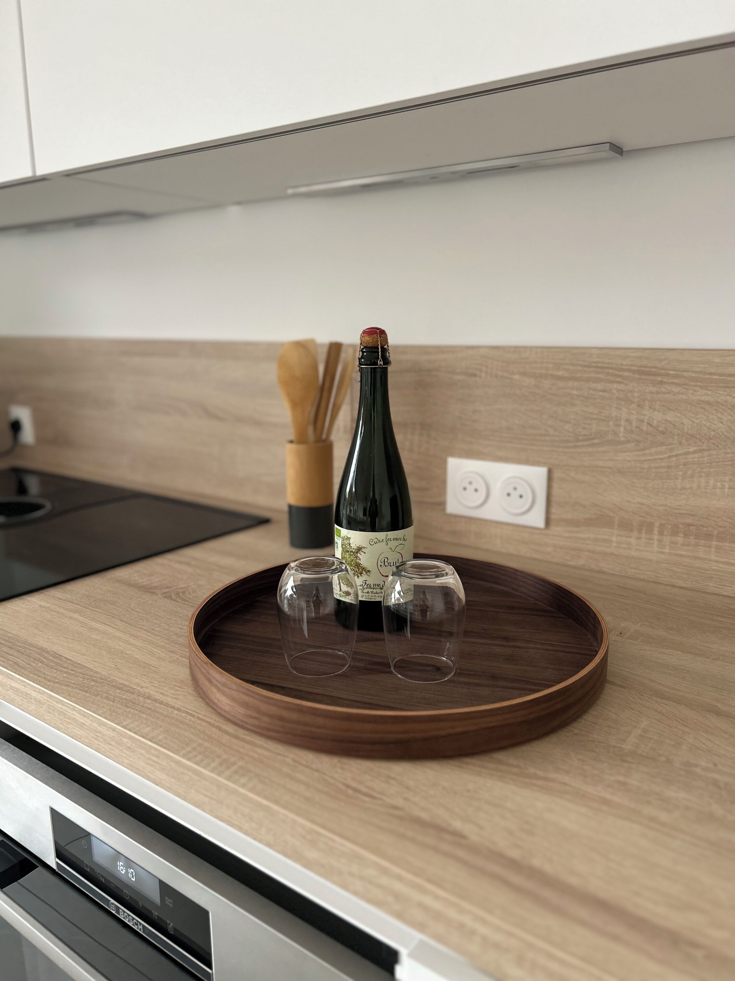 Een keukentafel met een houten dienblad waarop een fles en twee glaasjes staan.