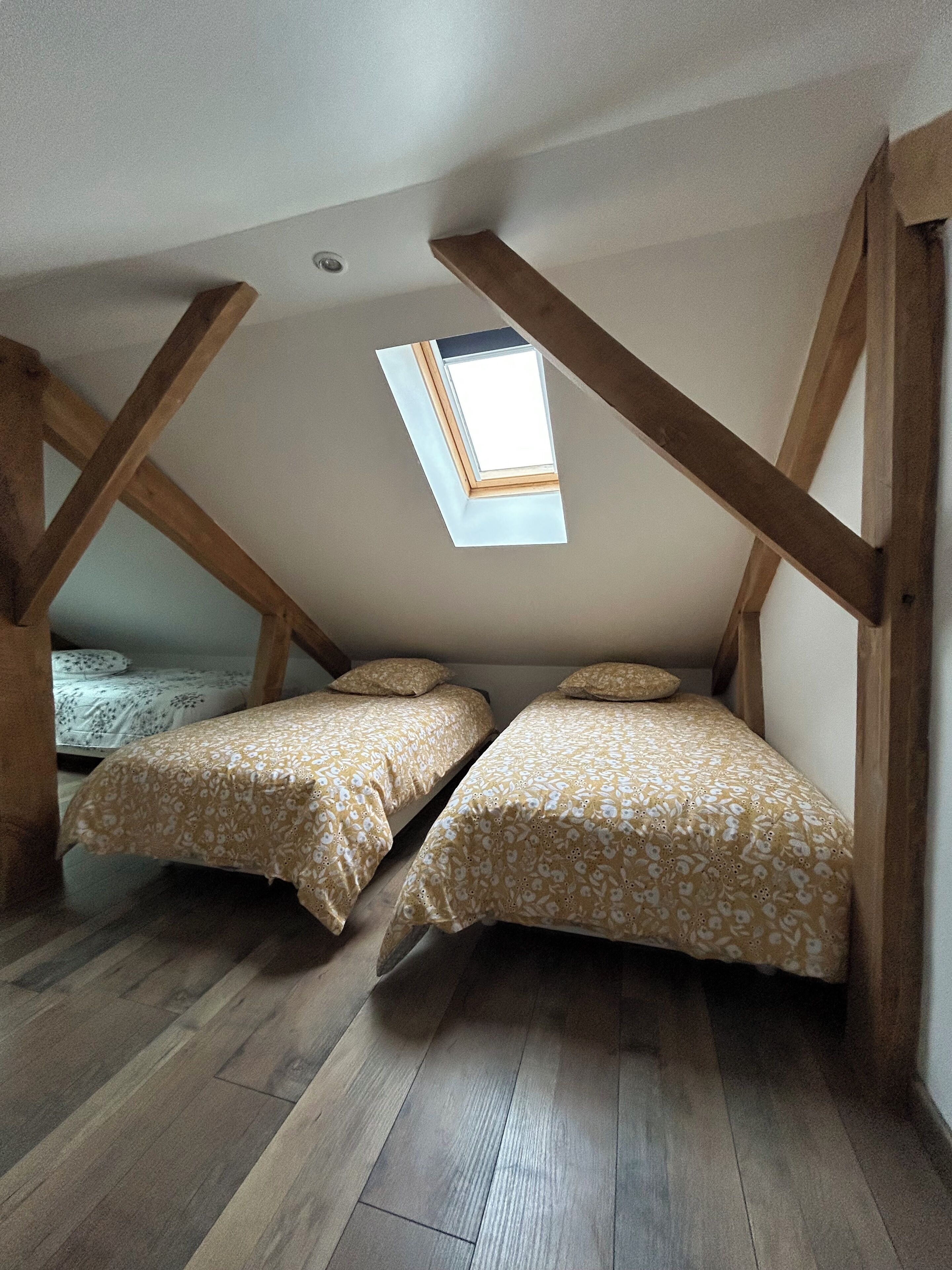 Un dormitorio en ático con dos camas, vigas de madera y un tragaluz.